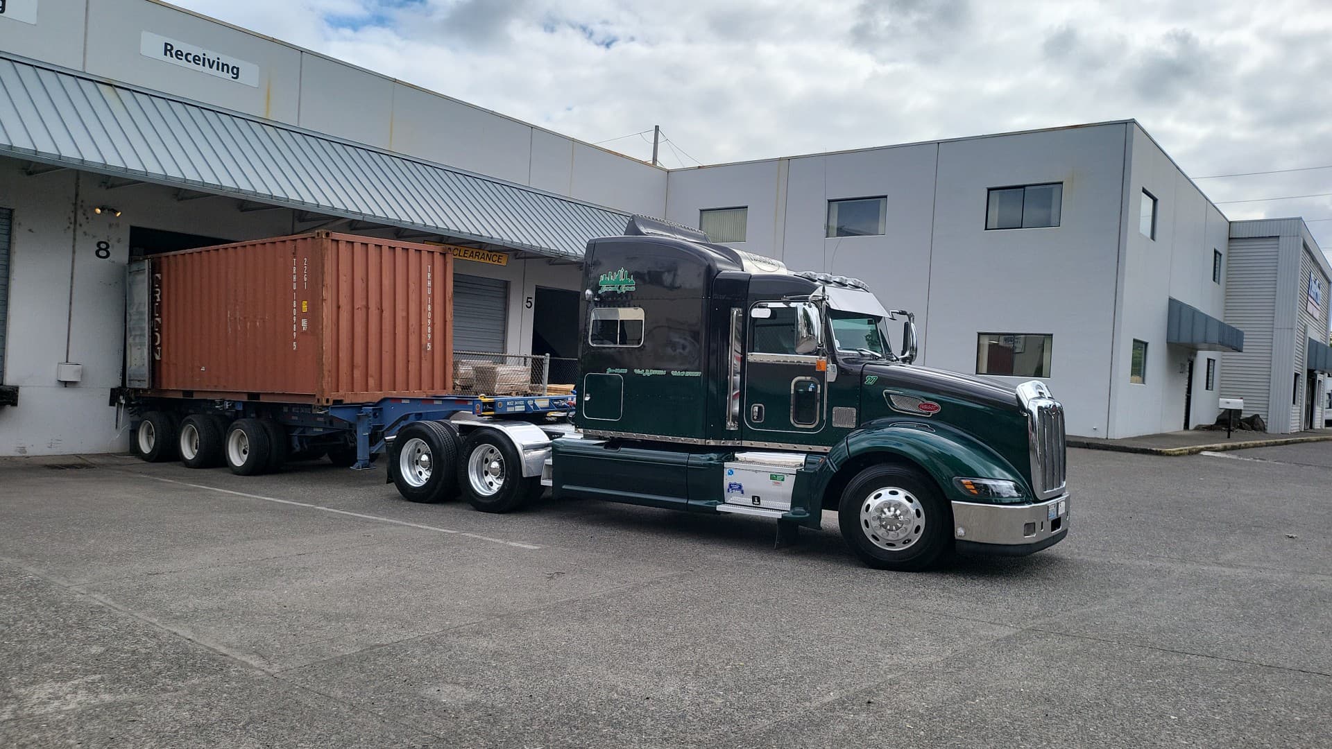 Emerald Express Peterbilt backing a 20-foot container into a receiving dock